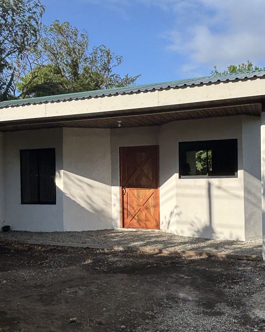 A finished house exactly as it came out of the phone: white facade, wooden door, gravel yard